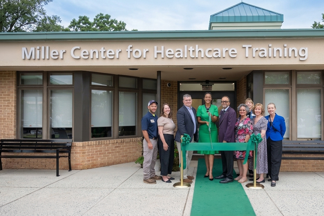 FCC leadership and staff pose for a ribbon-cutting outside the Miller Center for Healthcare Training, with a green ribbon and carpet leading to the entrance